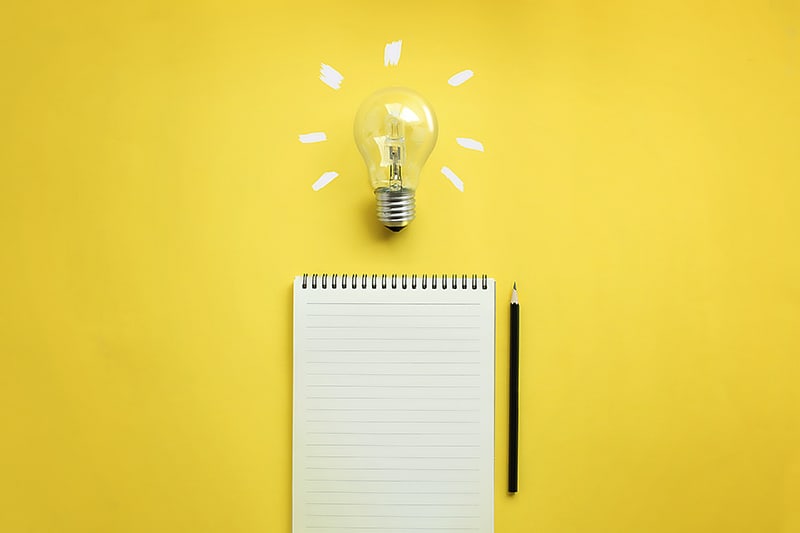 Flat lay of light bulb and empty memo pad and pencil